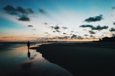 夕阳下，蓝色多云的天空下，人影在海边穿行